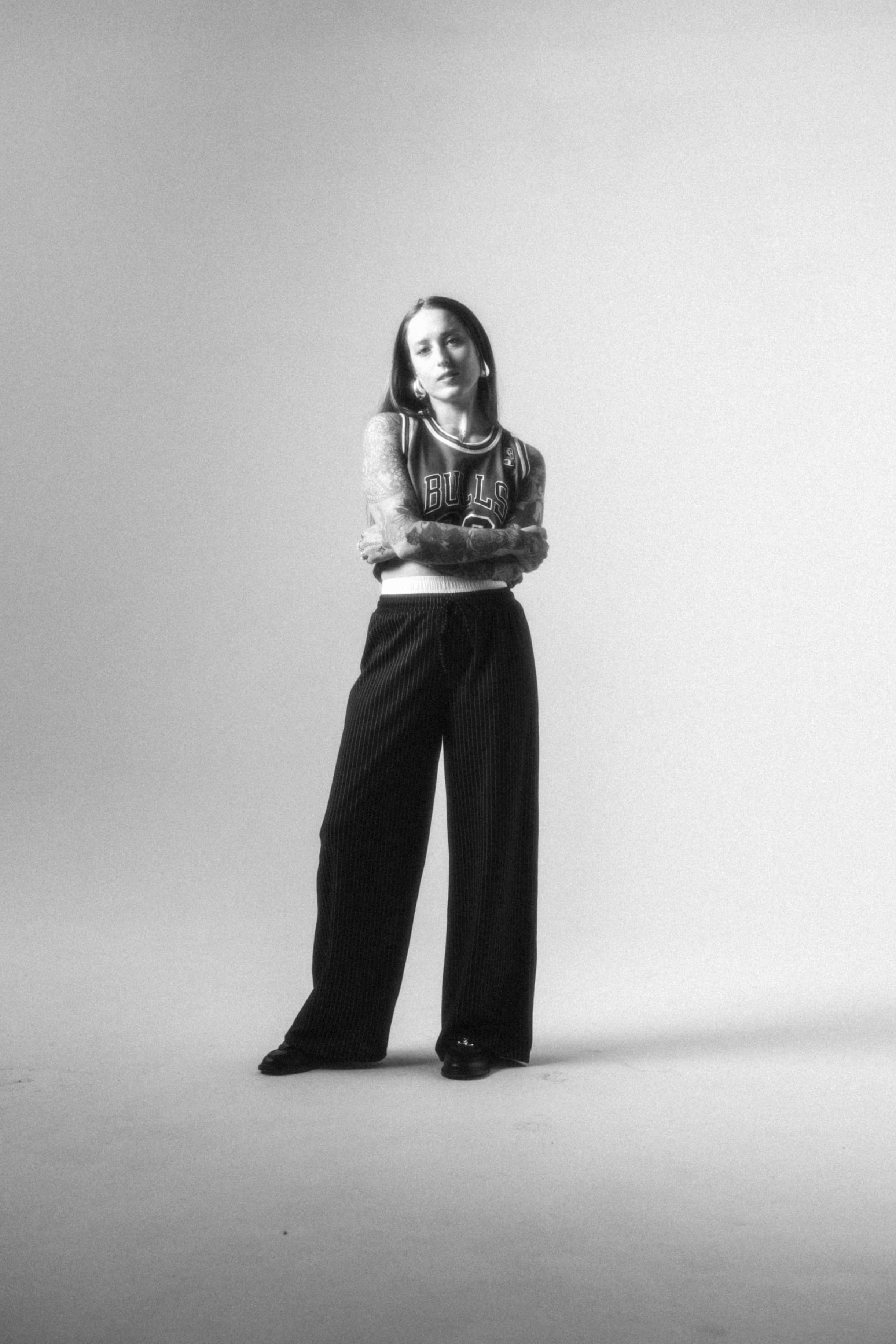 Full body professional photo of Libby George, in black-and-white. She’s wearing a fashionable outfit and has her arms crossed.